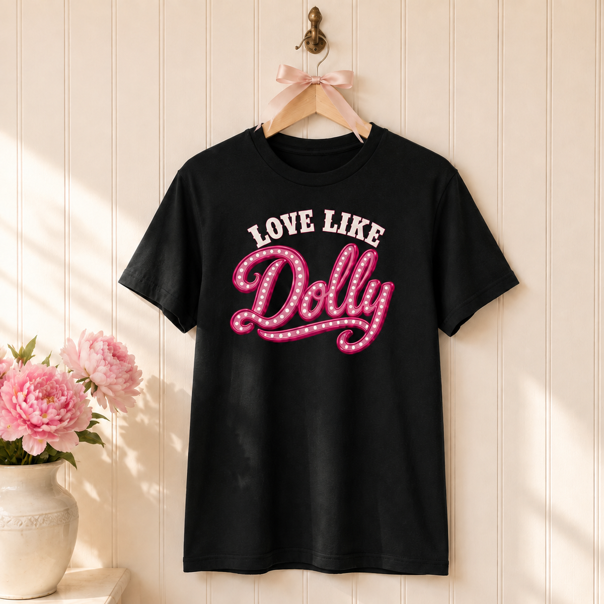 Black Love Like Dolly tee on a wooden hanger with a blush bow and pink flowers