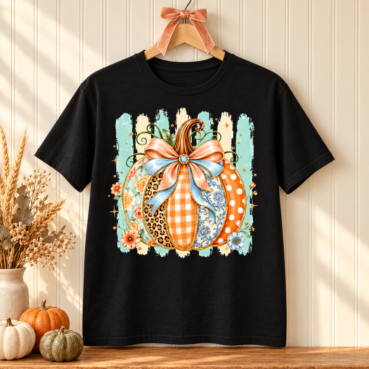 Black patchwork pumpkin graphic tee on a wooden hanger with fall décor