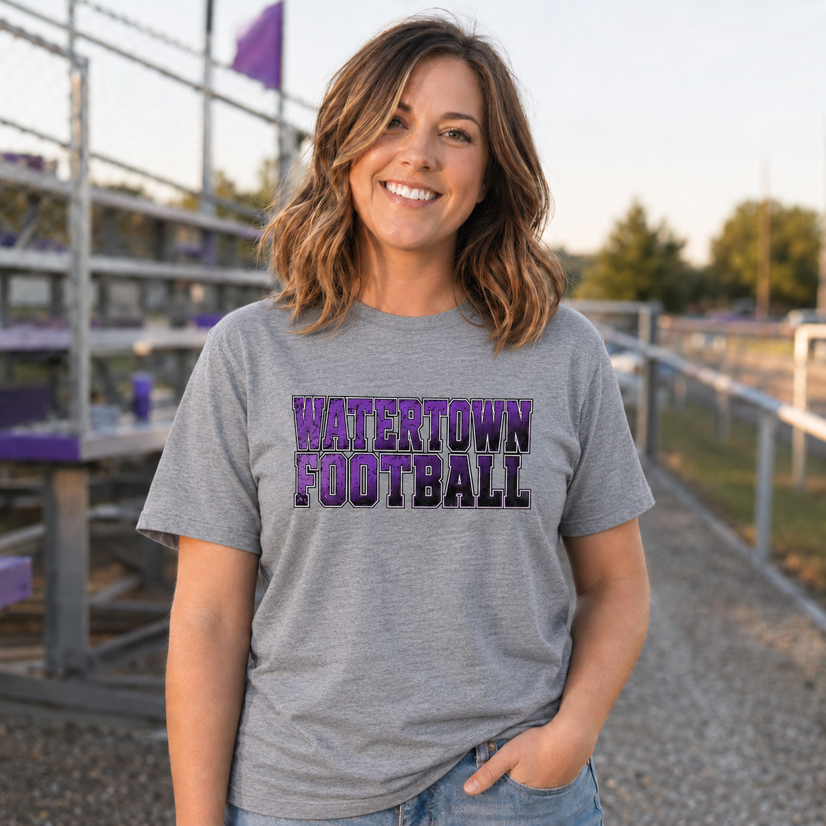 Woman wearing a heather gray Watertown Football graphic tee at football bleachers